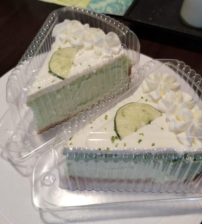 Two slices of More Than Pudding's key lime pie with whipped cream and lime in plastic containers.