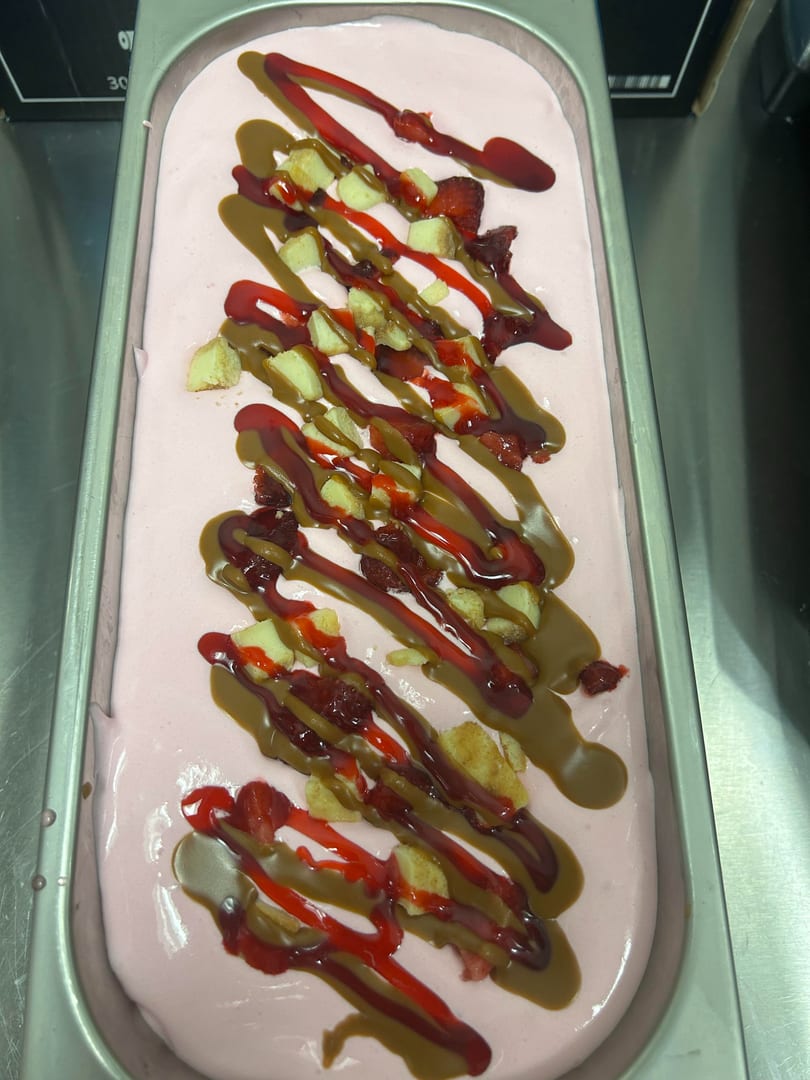 Pink dessert with drizzles of red and caramel sauces, topped with cake pieces and strawberries.